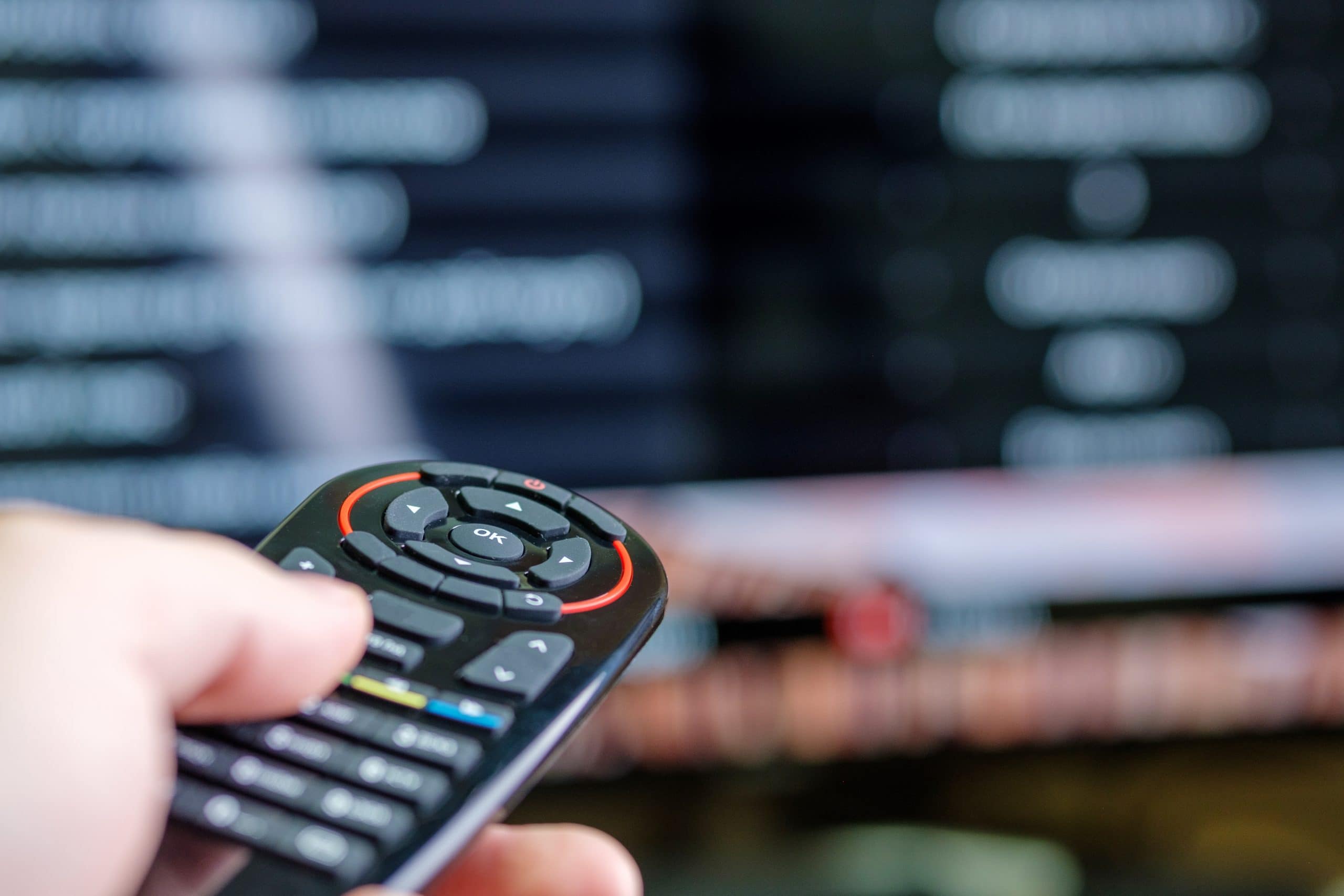 male hand holds a rounded tv remote control, blurred tv background